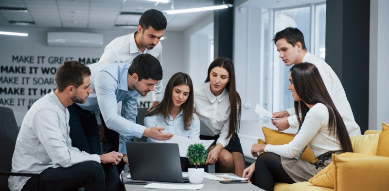 Guy shows document to a girl. Group of young freelancers in the office have conversation and working.